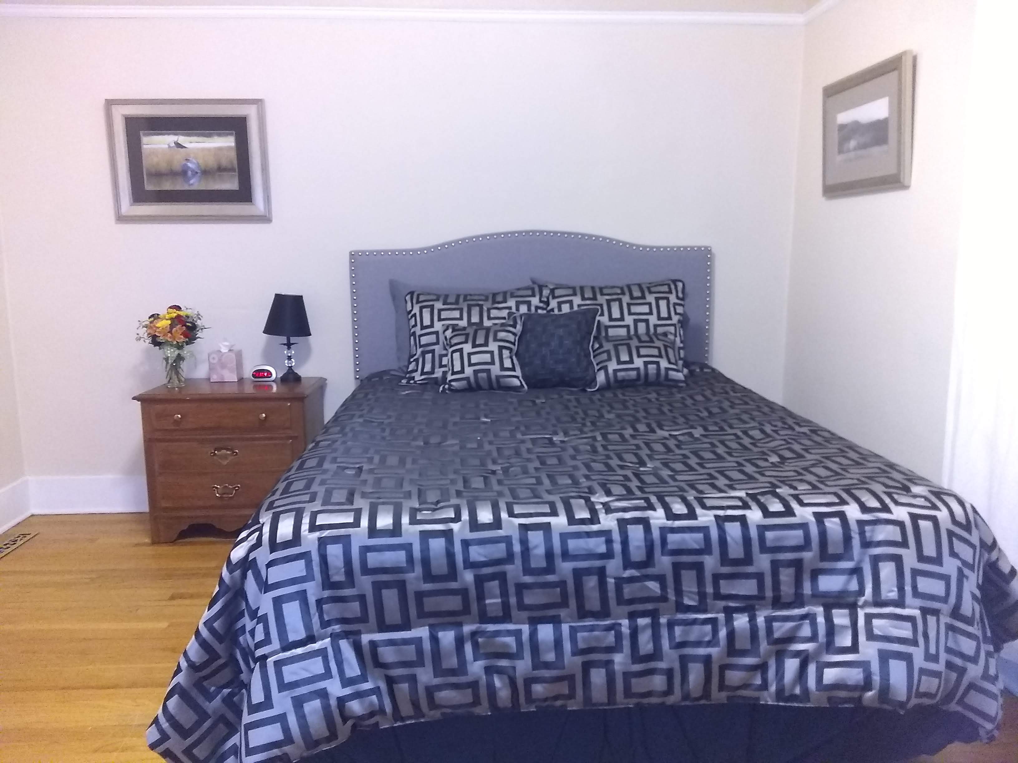 Queen bed in a large room with end table and hardwood floor