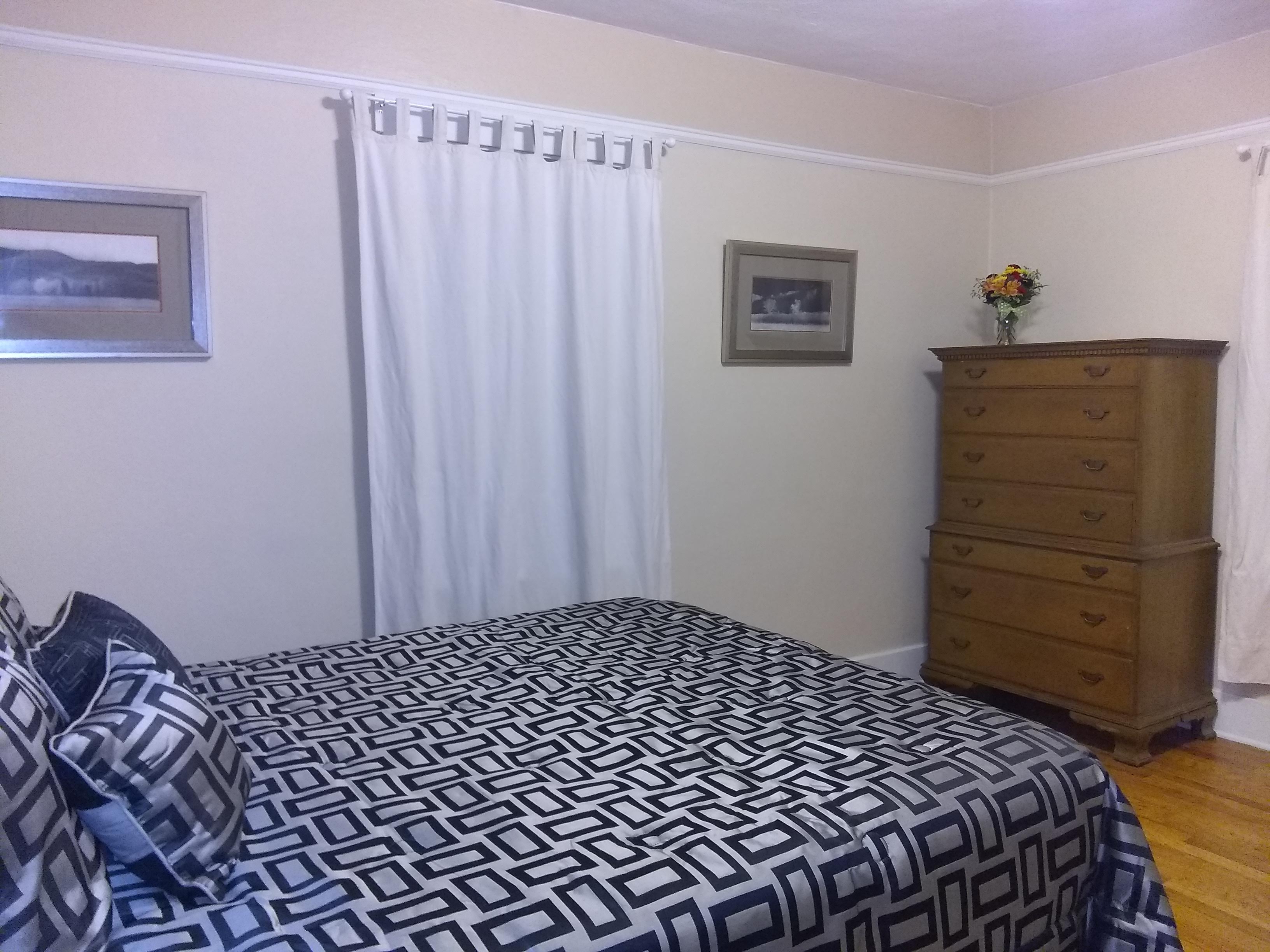 Queen bed in a large room with a dresser and hardwood floor